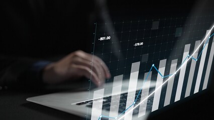 A business professional focuses on financial data displayed on a laptop, with dynamic graphs...