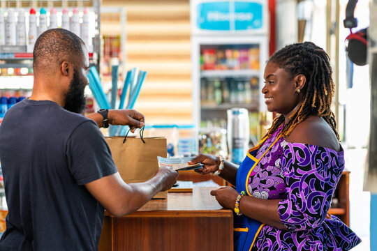 African businesswoman receives cash from a customer after purchase at her supermarket, local commerce and payment