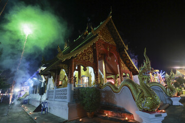 Serene Lanna style Thai temple at night during vibrant festival celebration. Mystical green smoke...