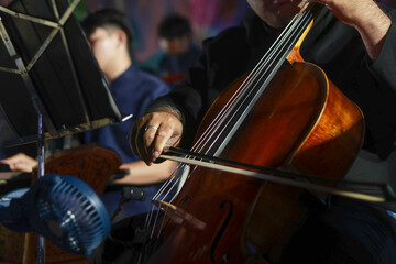 Fototapeta premium Focused musician playing cello in classical music orchestra concert. This passionate performance shows close up of hand, bow, and string instrument during symphony