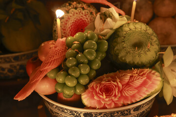 Warm, serene fruit offering in bowl with carved watermelon and lit candle. This sacred arrangement features grape, guava, and intricate food art for traditional ceremony