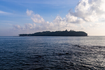 calm ocean and remote tree-covered island beneath gentle clouds