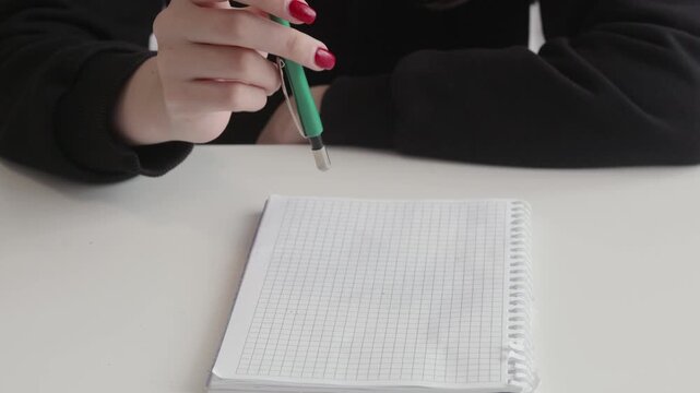 Woman with red manicure fidgeting and rhythmically tapping green mechanical pencil on desk, nervous habit or thinking gesture captured in closeup.