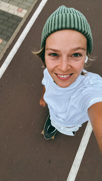 Young woman  rides a skateboard wearing green beanie on urban street