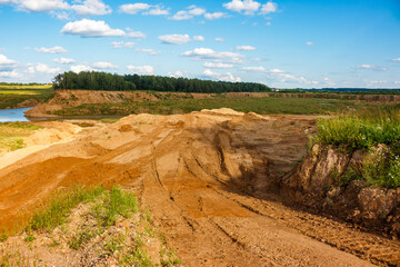 Vast open-pit sand quarry with freshly dug sand heaps and vehicle tracks under a bright summer sky, showcasing excavation and raw earth