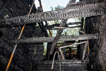 Charred wooden beams and walls of a destroyed house after a fierce fire. Devastated structure with...