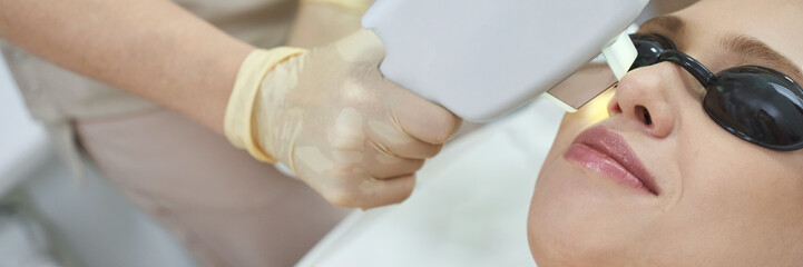 Young caucasian female undergoing laser skin treatment at dermatology clinic with protective goggles.