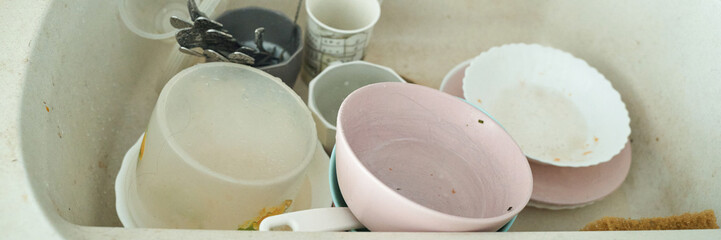 Dirty dishes in sink with mugs, plates, and cups highlighting unwashed utensils and cluttered kitchen environment.