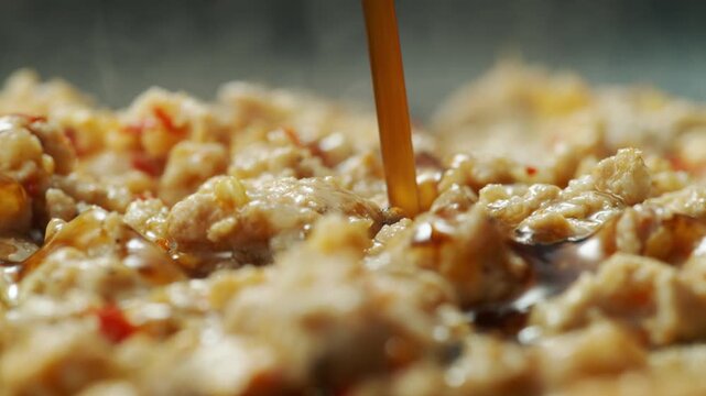 Close up oyster sauce pouring over sizzling minced pork in wok for Pad Krapow