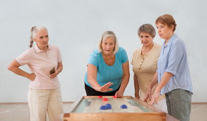 senior group Playing the board game of shuffleboard.  Kidult gaming in the gym. Active retirement...