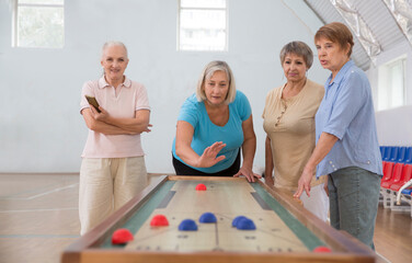 senior group Playing the board game of shuffleboard.  Kidult gaming in the gym. Active retirement...