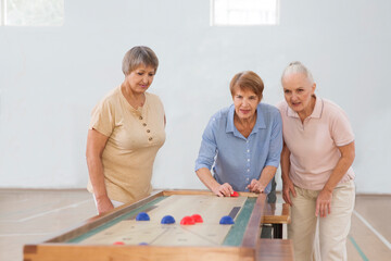 senior group Playing the board game of shuffleboard.  Kidult gaming in the gym. Active retirement...