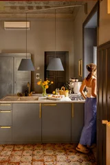 Woman enjoying a peaceful morning in a stylish Sicilian kitchen with vintage tiles, gray cabinets, and yellow flowers. Cozy Mediterranean home atmosphere © rh2010