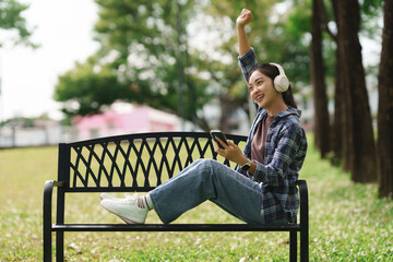 Young woman enjoying music headphones celebrating success in park