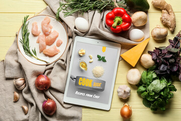 Tablet computer with tasty ingredients on yellow wooden background