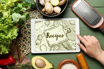 Woman using digital recipe book, different ingredients and kitchen utensils on green wooden...