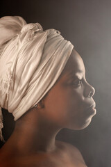 Profile portrait of beautiful Black woman with white headwrap and bare shoulders looking into the...