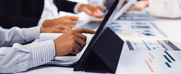 A group of professionals engage in a collaborative business meeting, analyzing data and developing strategies using laptops and documents on a bright office table. SACTR