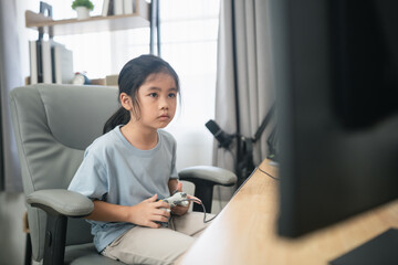 Young girl focused on video game console while sitting in a comfortable chair in a bright room with...