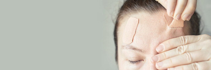 Female adult with bandages on forehead after injury or surgery with healing process on skin.