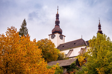 Church of the Transfiguration in Špania Dolina, a historic copper mining village, surrounded by autumn trees and traditional mountain architecture. © Marek