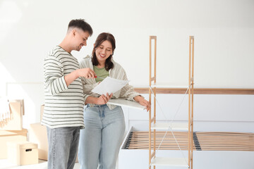 Young couple with instructions assembling shelving unit in bedroom on moving day
