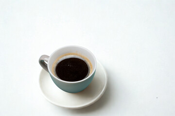 A single cup of dark coffee on a saucer against a white background