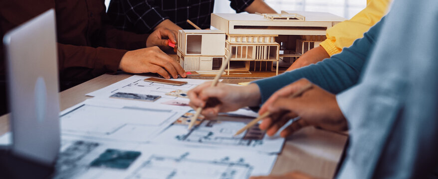A vibrant scene depicting a diverse group of architects collaborating on a design project, using blueprints and a physical model during an engaging planning session. SACTR - Powered by Adobe