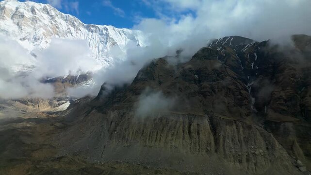 Majestic snow-covered peaks surrounded by drifting clouds near Tilicho Lake in Nepal, showcasing high-altitude mountain beauty with rocky slopes and dramatic Himalayan scenery.