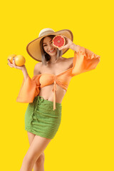 Beautiful young woman with grapefruits on yellow background