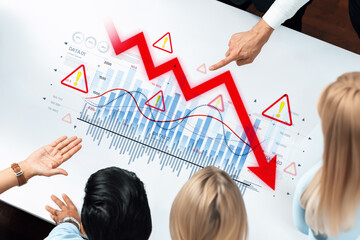 A diverse business team reviews a declining graph on a digital interface during a strategy meeting, focusing on risk indicators and trends affecting performance. Trope