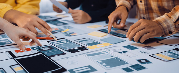 A vibrant scene captures a team collaborating on mobile app prototypes. Various hands engage with...