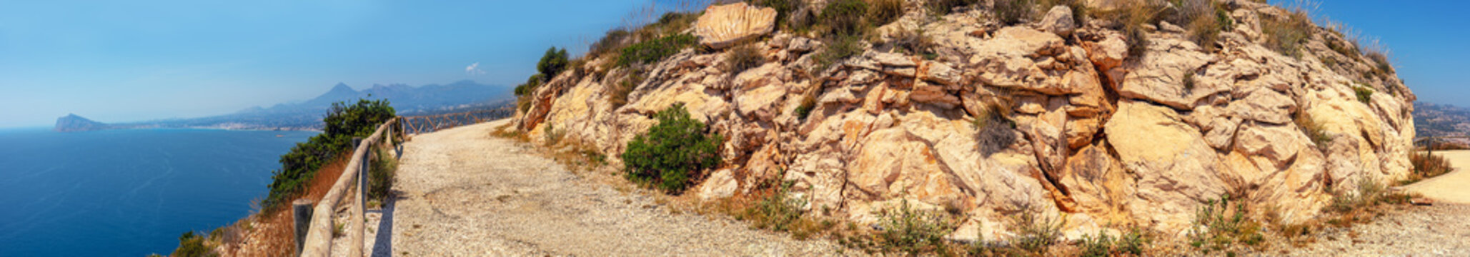 Panoramic view of the Mediterranean coast of Spain. Seascape with a rocky path around a mountain. High mountain road. Morro de Toix viewpoint. Calpe, Alicante, Spain