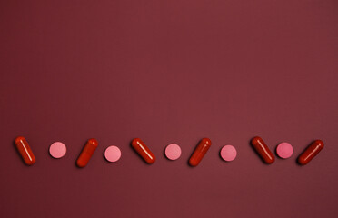 Various medical capsules are arranged in a row on a red background. Concept of medicine and patient treatment.
