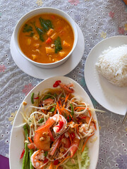 An authentic Thai meal featuring spicy Som Tum papaya salad with succulent shrimp, a hearty vegetable soup with baby corn and spinach, served alongside fluffy jasmine rice. A vibrant and flavorful