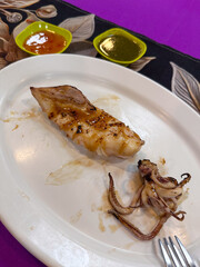 Delicious grilled squid, expertly prepared and served on a pristine white plate, accompanied by two vibrant dipping sauces. A perfect seafood appetizer or main course, highlighting fresh flavors and