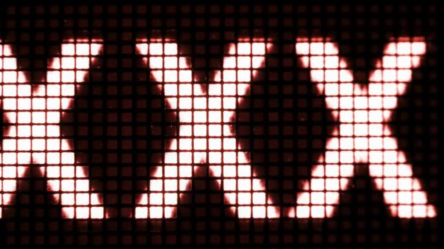 An extreme close-up macro video of blocky, pixelated 'XXX' text flashing red on white then white on red on a digital screen, emphasizing retro tech aesthetic and sharp pixels. Digital warning concept