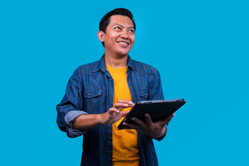 Young Man With Braces Joyfully Using Tablet While Looking Up With Bright Idea Over Blue Background