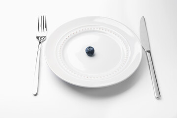 One blueberry on plate and cutlery on white table, closeup