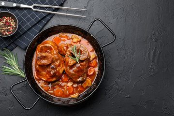 Tasty beef ossobuco with carrot and mushrooms served on dark textured table, flat lay. Space for text
