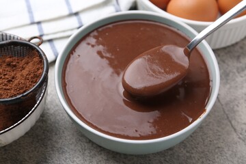 Liquid chocolate dough in bowl and ingredients on grey table, closeup