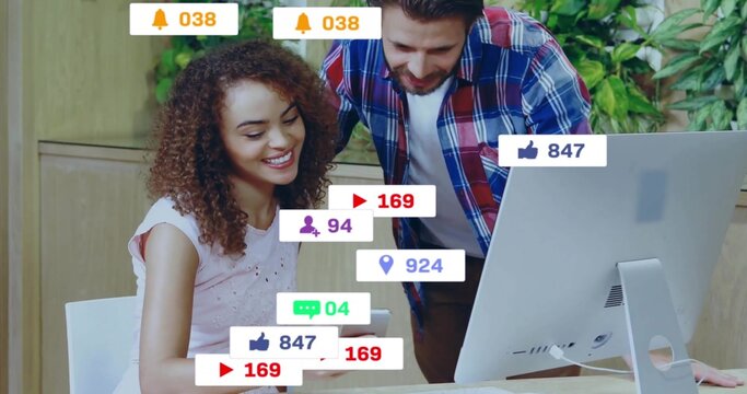 Smiling staff holding smartphone at desk as colleague leaning over monitor with notification icons