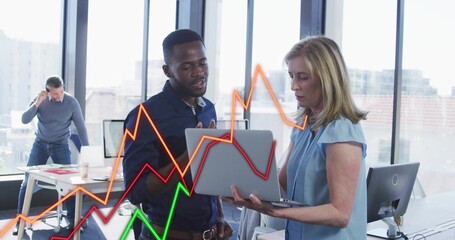 Reviewing two colleagues on laptop analyzing data in office space, with colored line chart overlays