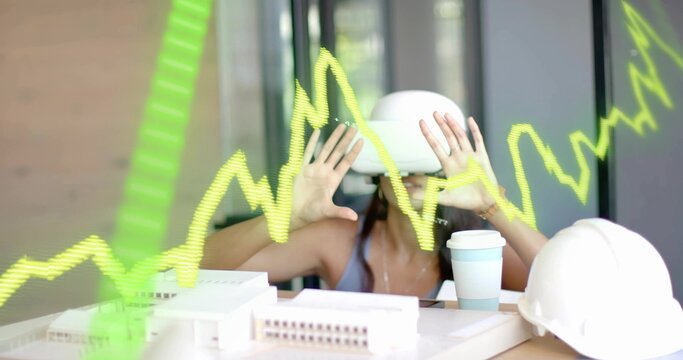 Woman wearing VR headset manipulating green graph overlay at office table, with model