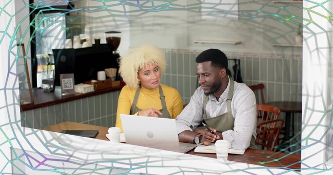 Collaborating baristas wearing aprons reviewing laptop content at cafe table with espresso machine