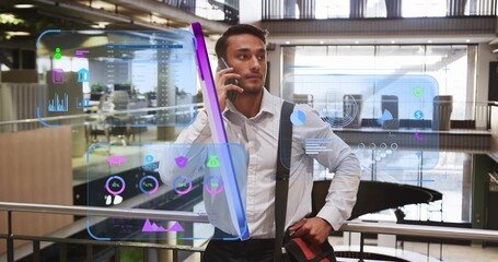 Analyzing charts, man in suit holding smartphone by railing at office atrium with messenger bag