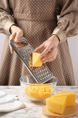 Woman grating cheese into bowl at white marble table, closeup