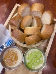Thai steamed bread served with two custard dips — rich pandan green custard and smooth Thai tea custard — presented in a wooden tray, showcasing a classic Thai dessert combination.