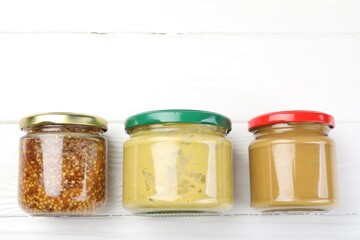 Jars with different tasty sauces on white wooden table, flat lay. Space for text