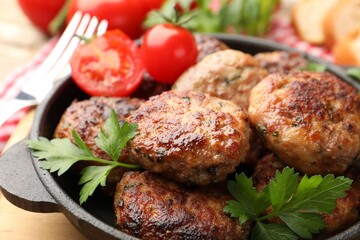 Delicious patties with parsley and tomatoes in pan on table, closeup